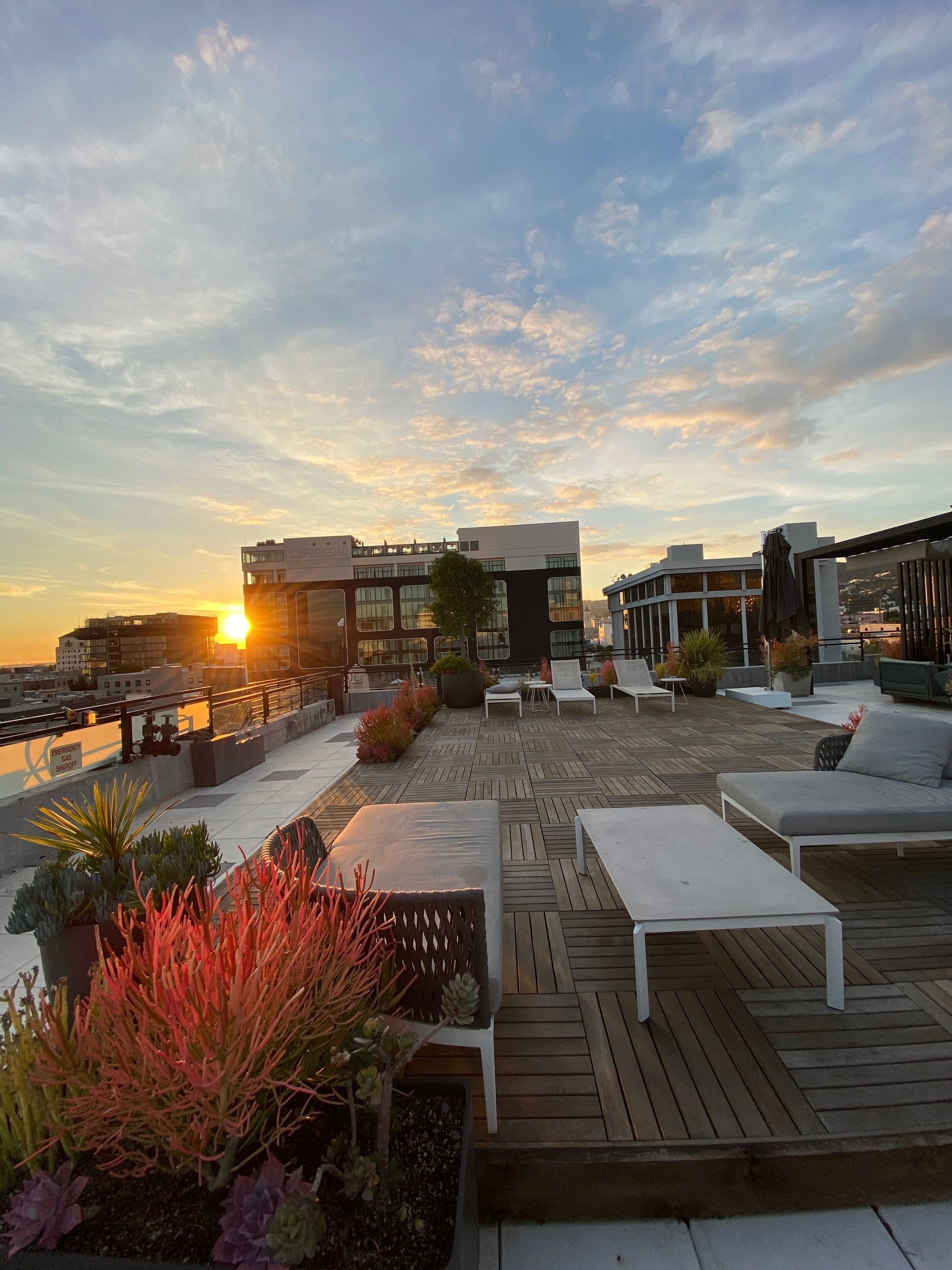 A rooftop terrace with outdoor seating, a view of the sunset, and a modern building in the background.