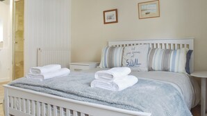 A neatly made bed with a striped pillow and a pillow with the text "Let your dreams set sail".