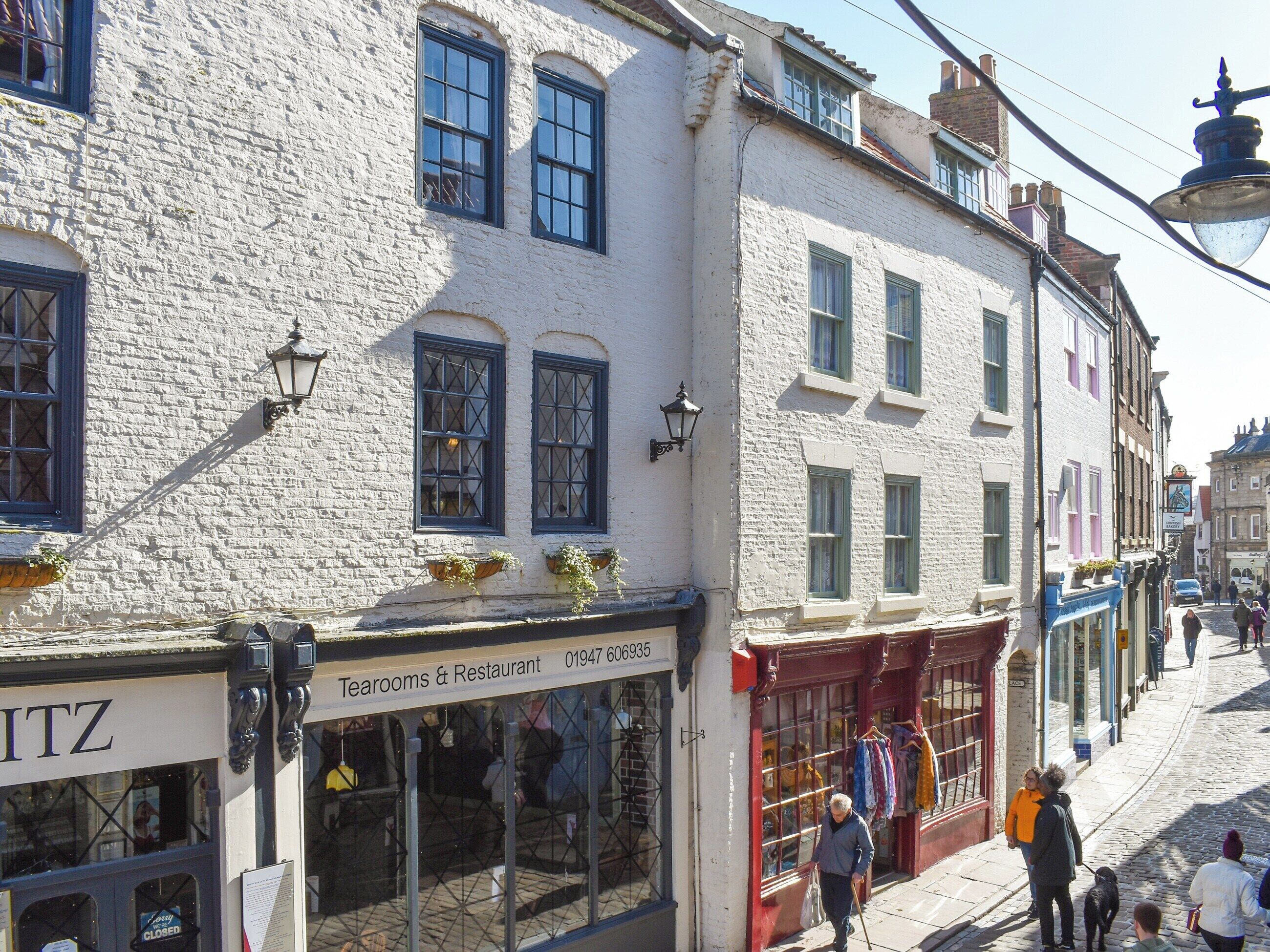 A street with buildings, a shop named "Teerooms & Restaurant", and people walking.