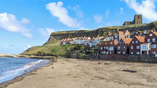A coastal town with a prominent castle on a hill, terraced houses, and a sandy beach.