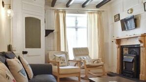 A living room with a sofa, two chairs, a table, a fireplace, and a television mounted above it.