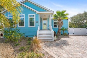 A blue house with a front porch, steps, and a palm tree.