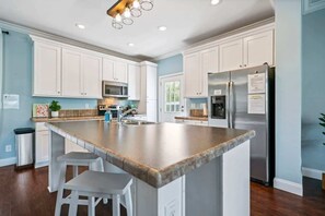A kitchen with white cabinets, a large island with stools, stainless steel appliances, and a ceiling light fixture.