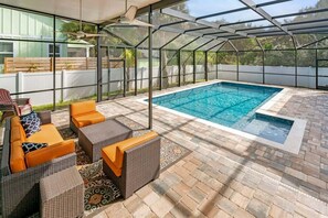 A covered outdoor swimming pool with wicker furniture and a patio area.