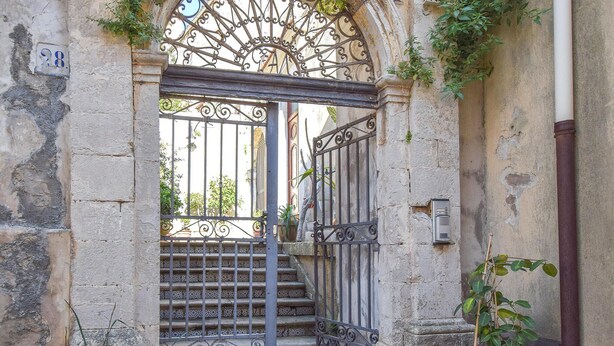 A wrought iron gate with a decorative arch, a stone wall, and a potted plant. - La casa dei Giarrentini (Modica)