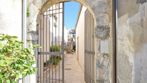An arched entrance with a metal gate, a stone wall, and a narrow pathway leading to a staircase. - La casa dei Giarrentini (Modica)