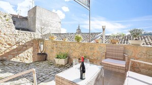A rooftop terrace with stone walls, potted plants, wicker furniture, and a bottle of wine on a table. - La casa dei Giarrentini (Modica)