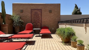 A terrace with red lounge chairs, a patterned wall, and potted plants. - Riad Shajara (Marrakech)