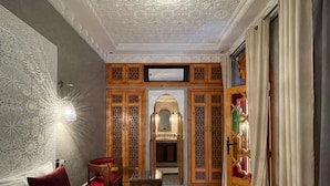 A hotel room with a large bed, a wooden chair, a small table, and a decorative wall. - Riad Shajara (Marrakech)
