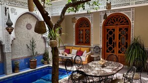 An outdoor patio with a pool, seating area, and decorative elements. - Riad Shajara (Marrakech)