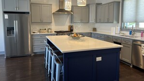 Una cocina moderna con armarios grises, un refrigerador de acero inoxidable, una isla central con taburetes e iluminación colgante.
