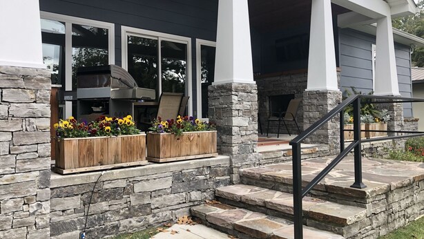 Una casa moderna con fachada de piedra, un ventanal grande y una zona de barbacoa integrada.