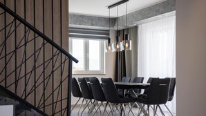 A modern dining area with a round table and black chairs, a staircase with a geometric design, and a large window with curtains.