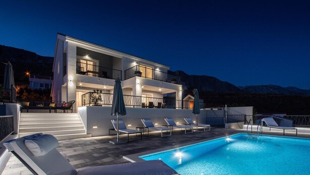 A modern two-story building with a swimming pool, outdoor seating, and a mountain backdrop.