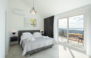 Ein modernes Schlafzimmer mit einem großen Bett, Blick ins Freie und einem Balkon mit Tisch und Stühlen.