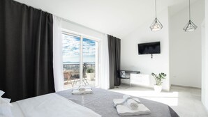 A modern hotel room with a large bed, a balcony with a view, a flat-screen TV, and a minimalist decor.