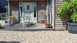 A wooden house with a porch, a metal chair, and two potted plants. - The Old Dairy At Wooton - UKC4355 (East Chiltington)