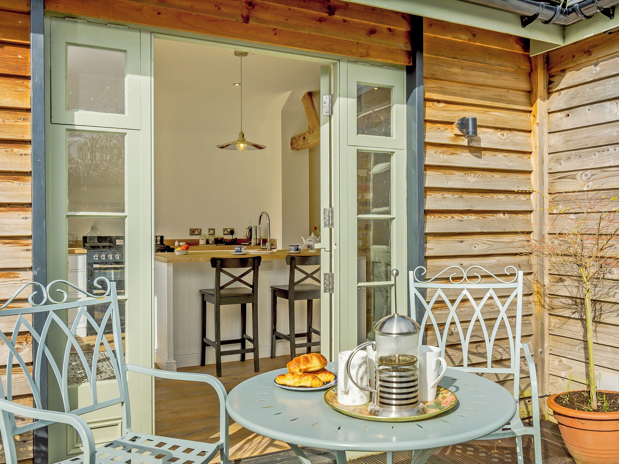 Un espace extérieur accueillant, avec une table et des chaises, une cafetière et une assiette de croissants.