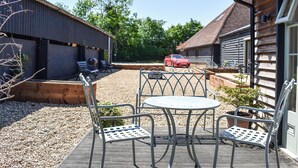A patio with metal chairs and a table, a red sports car parked in the background, and wooden buildings with a sloped roof. - The Old Dairy At Wooton - UKC4355 (East Chiltington)