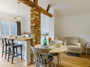 Een gezellige keuken met een bakstenen zuil, houten balken, een eethoek met een ronde tafel en een gestoffeerde fauteuil.