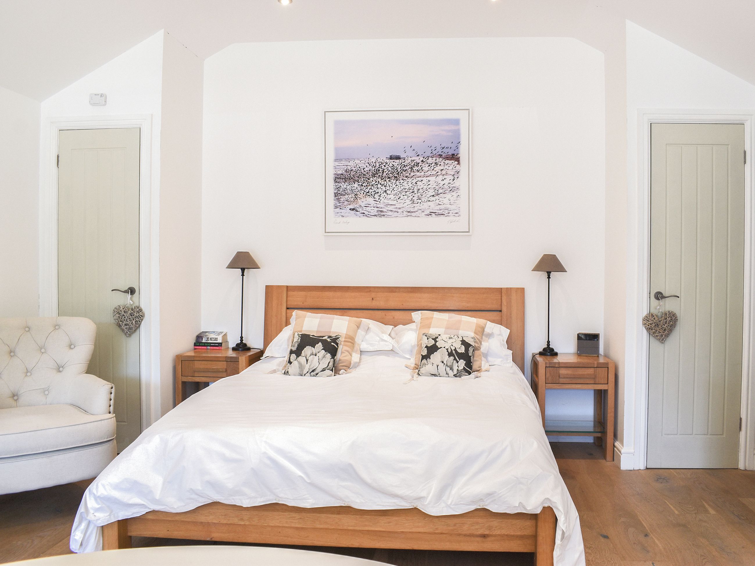 Una camera da letto con un letto in legno, biancheria bianca, due lampade da comodino, una decorazione a forma di cuore e un quadro appeso al muro.