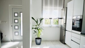 Una cucina moderna con mobili bianchi, un frigorifero in acciaio inox e un forno integrato. Al centro, una pianta in vaso.