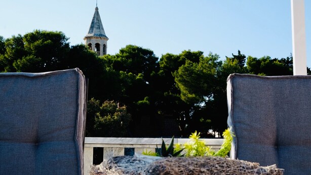 Ein Blick auf einen Kirchturm mit Kreuz, umgeben von üppigen, grünen Bäumen.