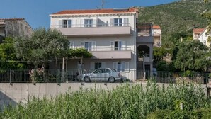 A two-story building with a red-tiled roof, a balcony, and a car parked in front.