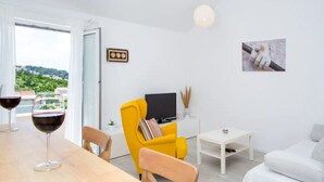 A modern living room with a wooden dining table, yellow armchair, white sofa, and a TV on a white stand.