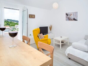 Un salon moderne avec une table à manger en bois, un fauteuil jaune, un canapé blanc et un téléviseur posé sur un meuble blanc.