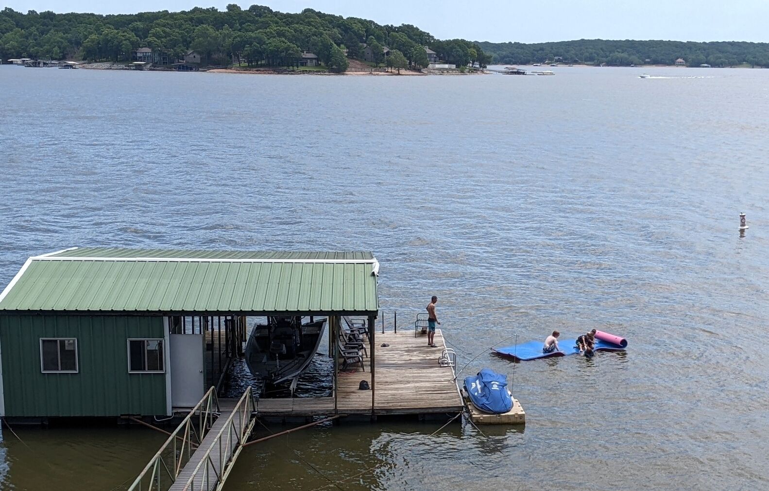 A dock with a green building, a boat, and a person on a paddleboard.