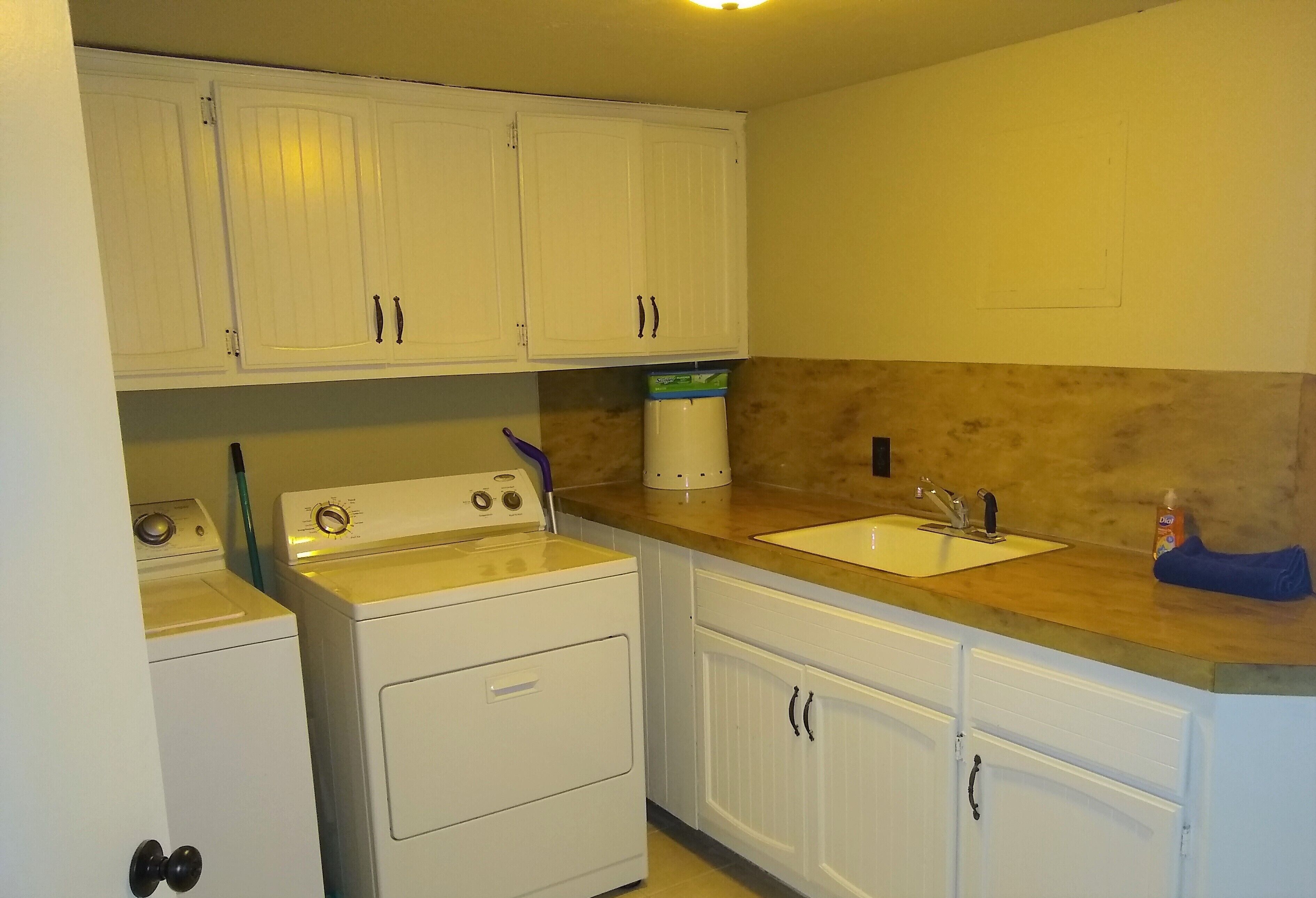A compact kitchen with white cabinets, a washing machine, a sink, and a countertop with a bottle of dish soap.