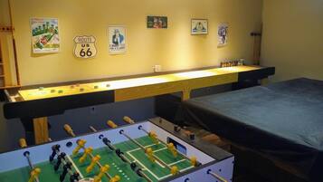 Une pièce avec une table de baby-foot, un lit et un bureau avec une lampe. Il y a des affiches au mur, dont une représentant la « Route 66 » et une autre avec le slogan « On vous veut dans l’armée américaine ».