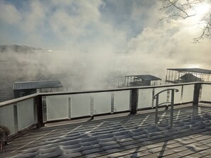 Een terras aan het water met een reling, een helder zicht op het meer en verschillende overdekte constructies.