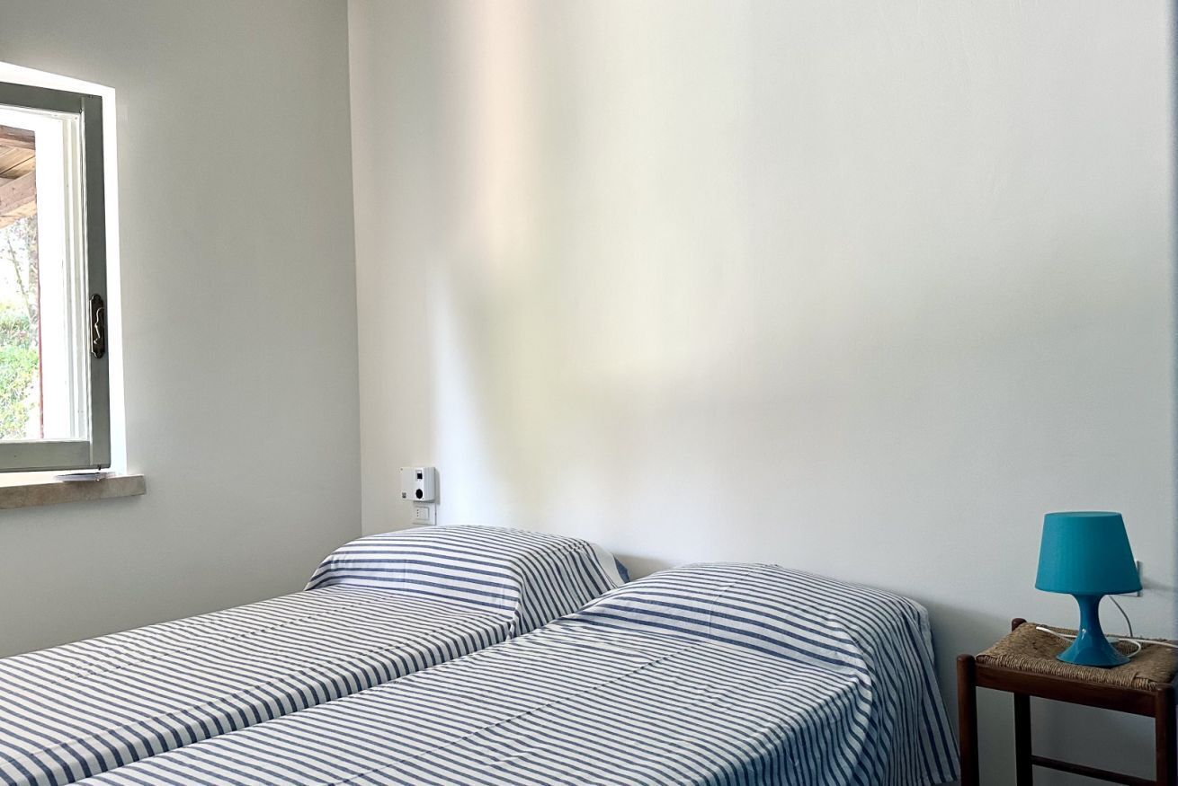A room with two beds, a window, a lamp, and a wall socket.
