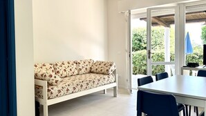 A room with a white sofa, a dining table with chairs, and a large window with a view of greenery. - N081 - Numana, villa with garden (Numana)