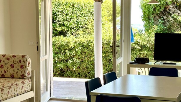 A room with a sofa, a table, chairs, a TV, and a view of a green hedge outside. - N081 - Numana, villa with garden (Numana)