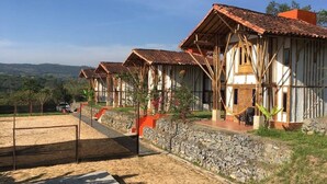 A row of rustic wooden cabins with tiled roofs, a stone wall, and a concrete patio area. - Hotel La Montoya (Curiti)