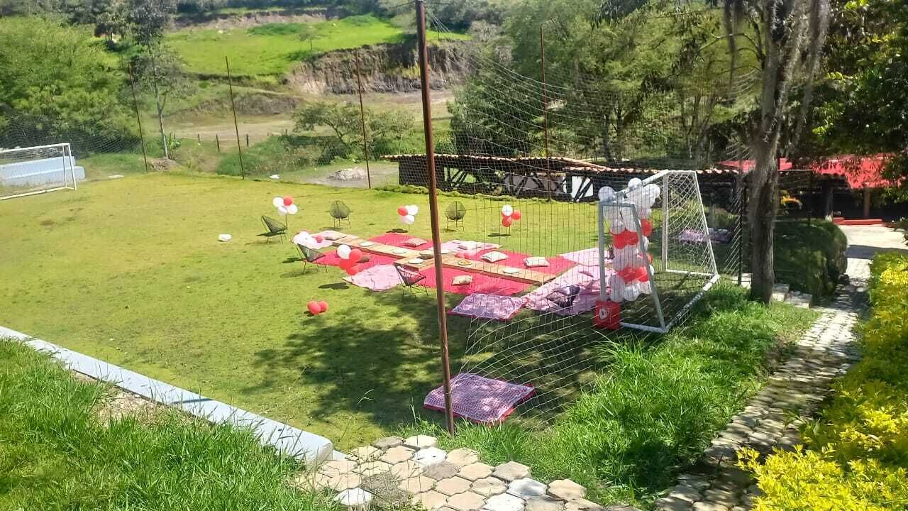 A grassy outdoor area with a picnic setup, including tables and chairs, and a soccer goal in the background.