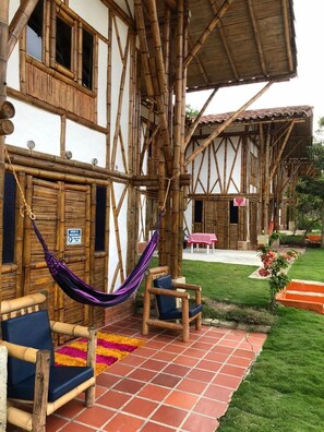 A traditional wooden building with a tiled patio, a hammock, and outdoor seating. - Hotel La Montoya (Curiti)