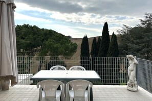 A terrace with a table and chairs, a statue, and a view of trees and hills.