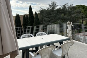 A terrace with a table and chairs, a statue, and a view of trees and hills. - M213 - Marcelli, three-room apartment with large panoramic terrace (Marcelli)