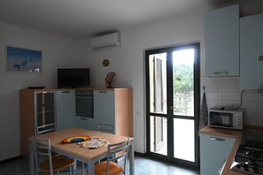 A compact kitchen with a dining area, a TV, and a view through the door.