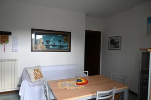 A dining area with a table, chairs, a framed painting, a radiator, and a pillow with text.