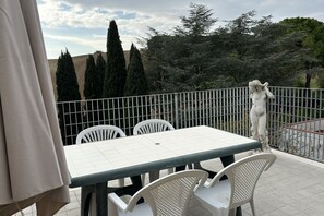 A terrace with a table and chairs, a statue, and a view of trees and hills.