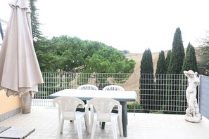 A patio with a table and chairs, a statue, and a view of trees and hills.