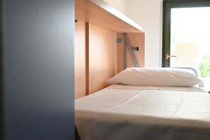 A single bed with a white pillow and a wooden headboard in a room with a door and a window.