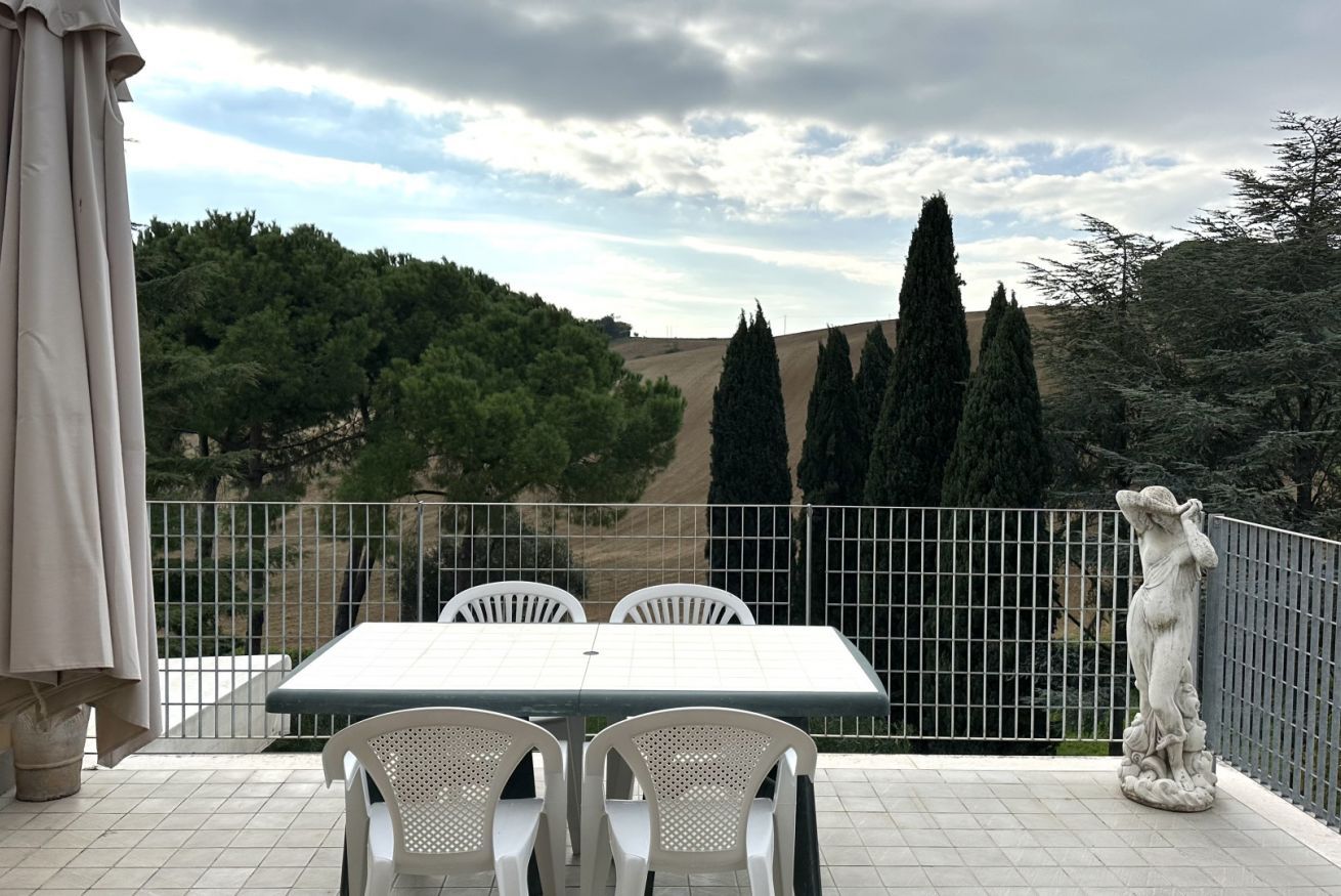 A terrace with a table and chairs, a statue, and a view of trees and hills.