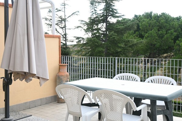 An outdoor patio with a table and chairs, a pergola with a canopy, and a decorative vase.