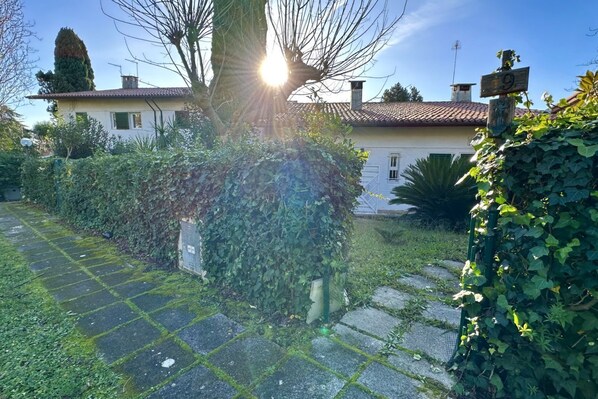 Ein Haus mit Ziegeldach, einer Hausnummer und einem Garten mit Baum und Hecke.